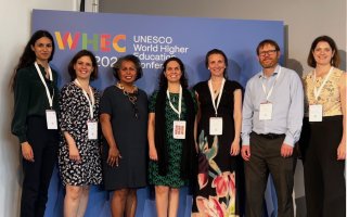 Seven people standing in front of the WHEC2022 conference banner